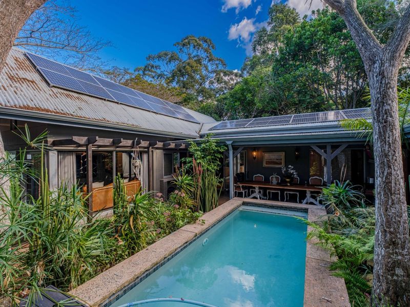 A private outdoor pool area featuring a stone-edged swimming pool, timber pergola, and solar panels installed on the corrugated metal roof.