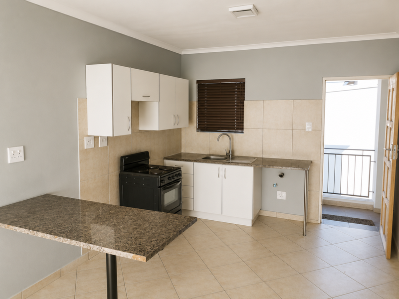 A clean, functional kitchen featuring granite countertops, white cabinetry, a freestanding stove, and tiled flooring, with direct access to an outdoor balcony.