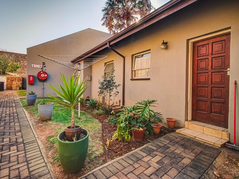 Front exterior view of the townhouse featuring a paved walkway, timber entrance door, and functional fire safety equipment.