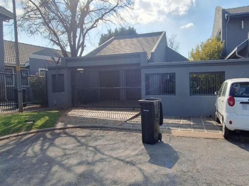 Front exterior view of the property featuring a paved driveway, secure perimeter wall, and gated entrance.