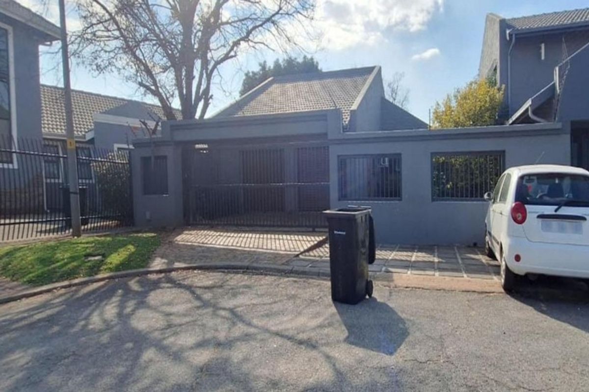 Front exterior view of the property featuring a paved driveway, secure perimeter wall, and gated entrance.
