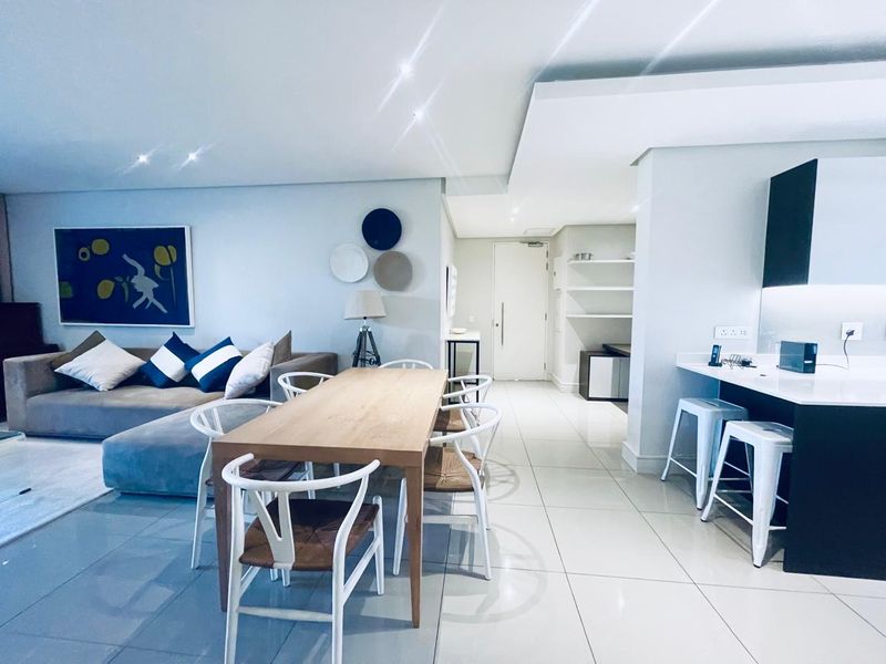 Modern open-plan living area featuring tiled floors, recessed lighting, and a sleek kitchen with a breakfast island and built-in cabinetry.