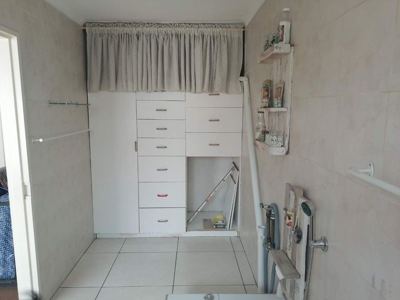 A functional laundry area featuring built-in cabinetry, tiled surfaces, and plumbing connections, offering potential for modernization and improved storage organization.