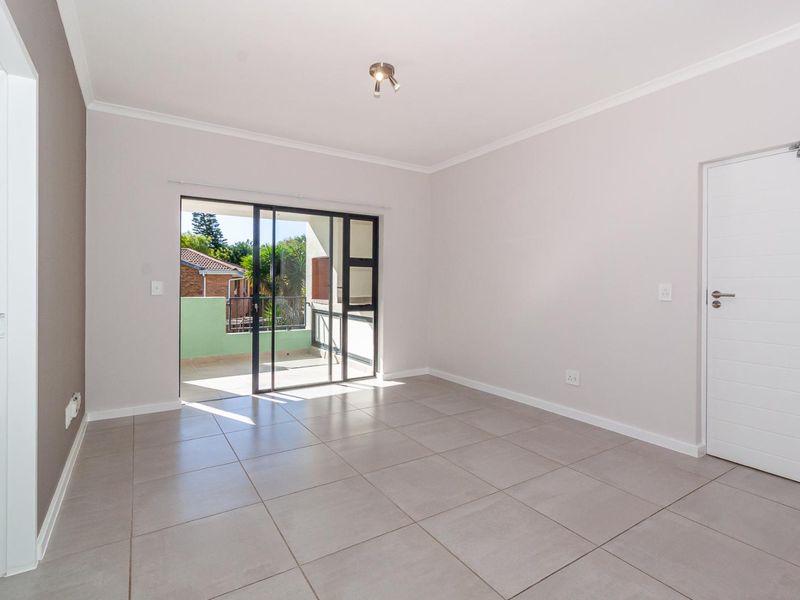 A bright, empty living room featuring neutral tiled flooring and a sliding glass door that opens onto a private balcony.