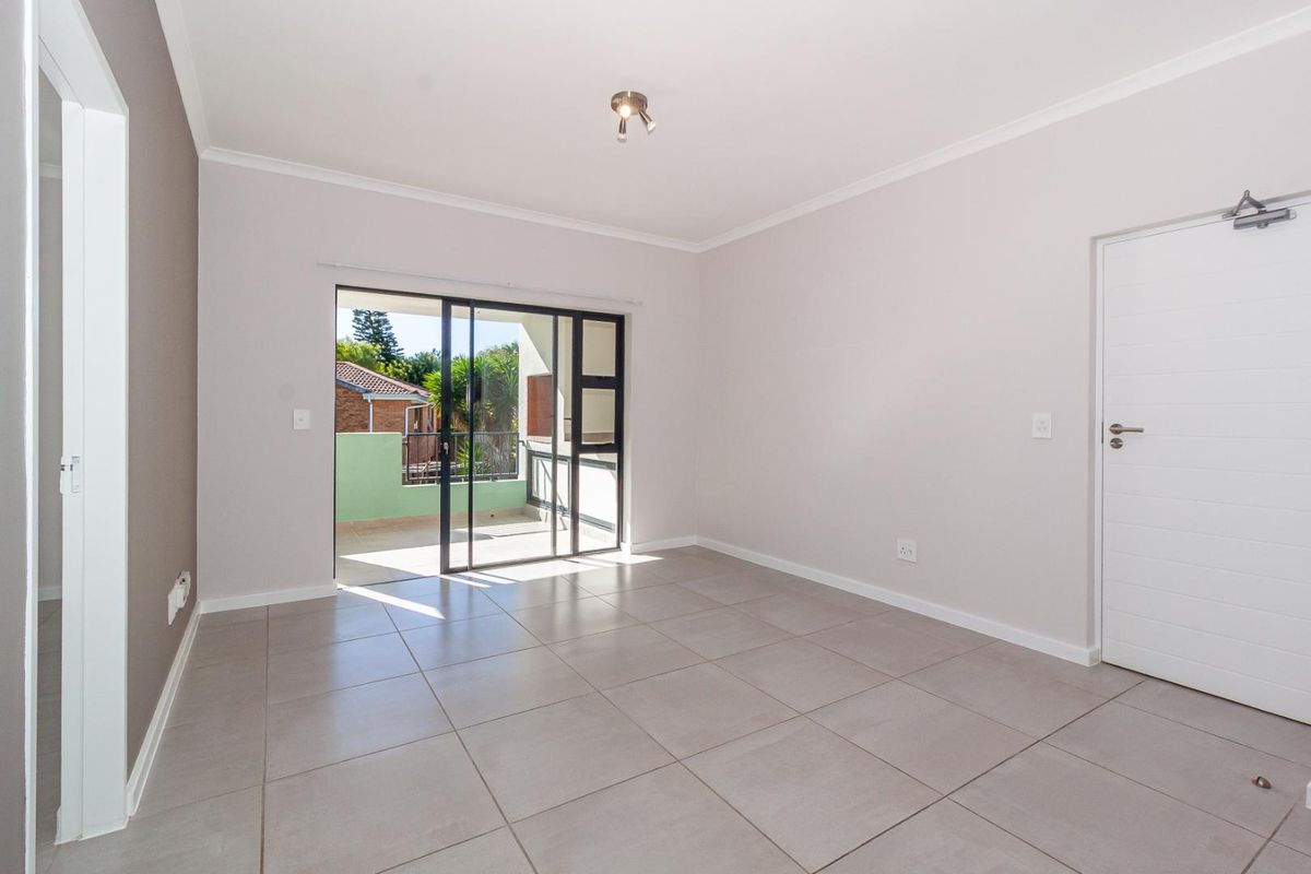 A bright, empty living room featuring neutral tiled flooring and a sliding glass door that opens onto a private balcony.