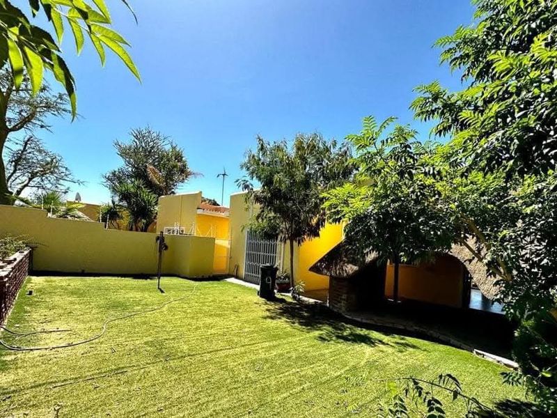 A private rear garden featuring a well-maintained lawn, perimeter boundary walls, and a traditional thatched lapa area for outdoor relaxation.