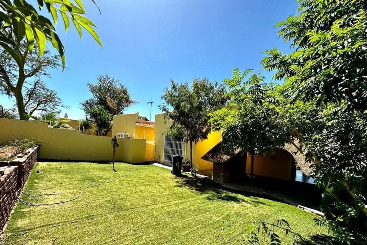 A private rear garden featuring a well-maintained lawn, perimeter boundary walls, and a traditional thatched lapa area for outdoor relaxation.