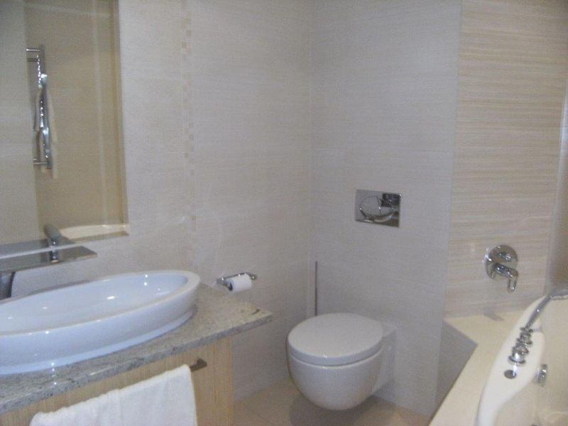 Modern bathroom featuring a wall-mounted toilet, vessel sink on a granite vanity, and a built-in bathtub with chrome fixtures.