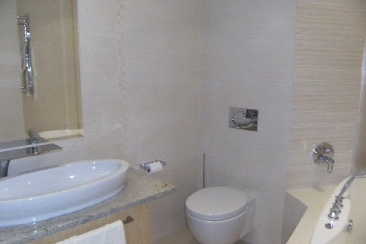 Modern bathroom featuring a wall-mounted toilet, vessel sink on a granite vanity, and a built-in bathtub with chrome fixtures.
