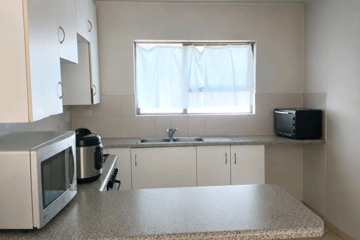 A functional kitchen featuring white cabinetry, laminate countertops, a double basin sink, and tiled flooring with a neutral backsplash.