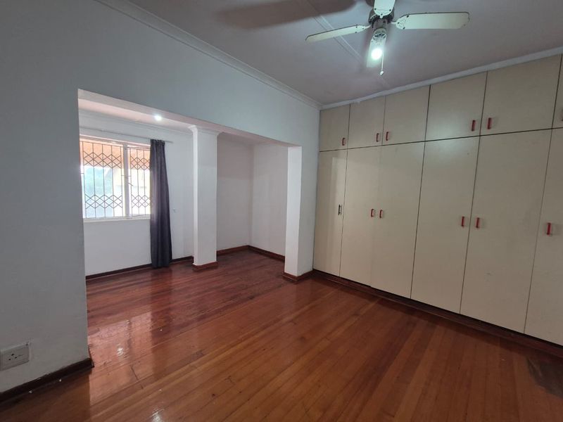 Spacious bedroom featuring polished hardwood flooring, extensive built-in cupboard storage, and a ceiling fan, offering a blank canvas for personalization.