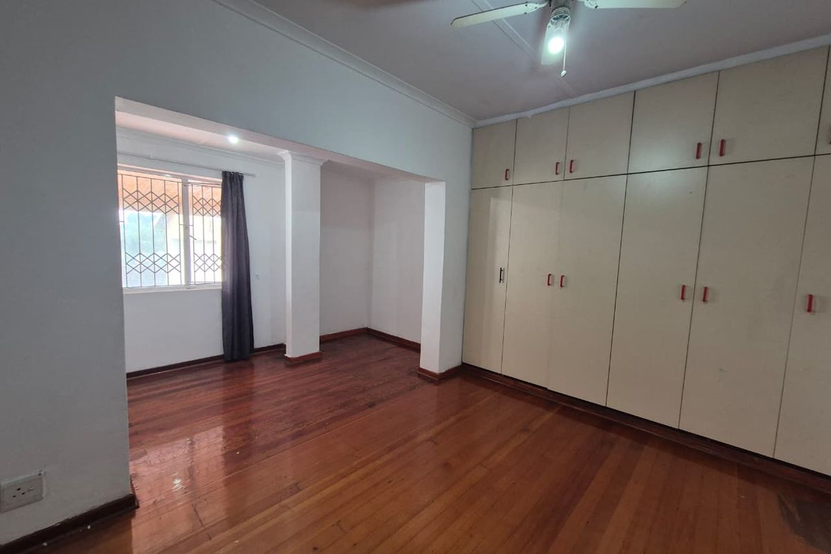 Spacious bedroom featuring polished hardwood flooring, extensive built-in cupboard storage, and a ceiling fan, offering a blank canvas for personalization.