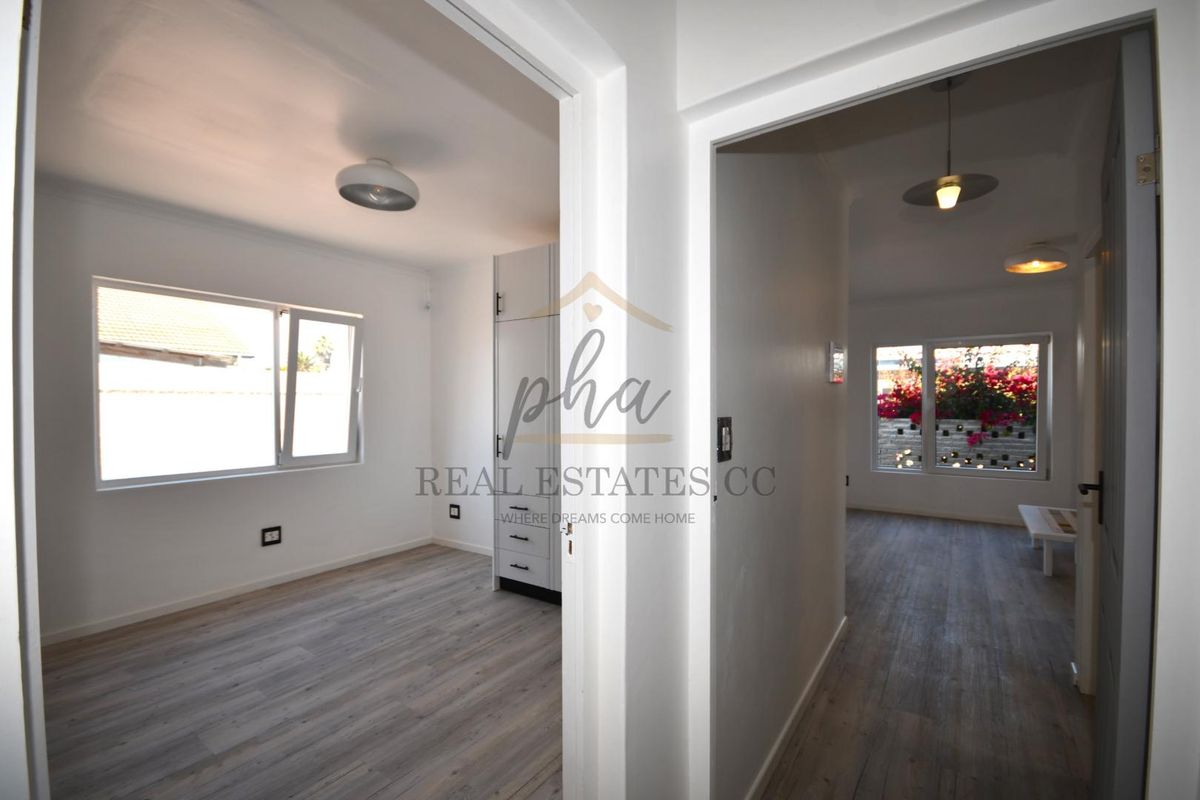 A bright, neutral bedroom featuring modern laminate flooring, built-in cabinetry, and large windows that allow for ample natural light.