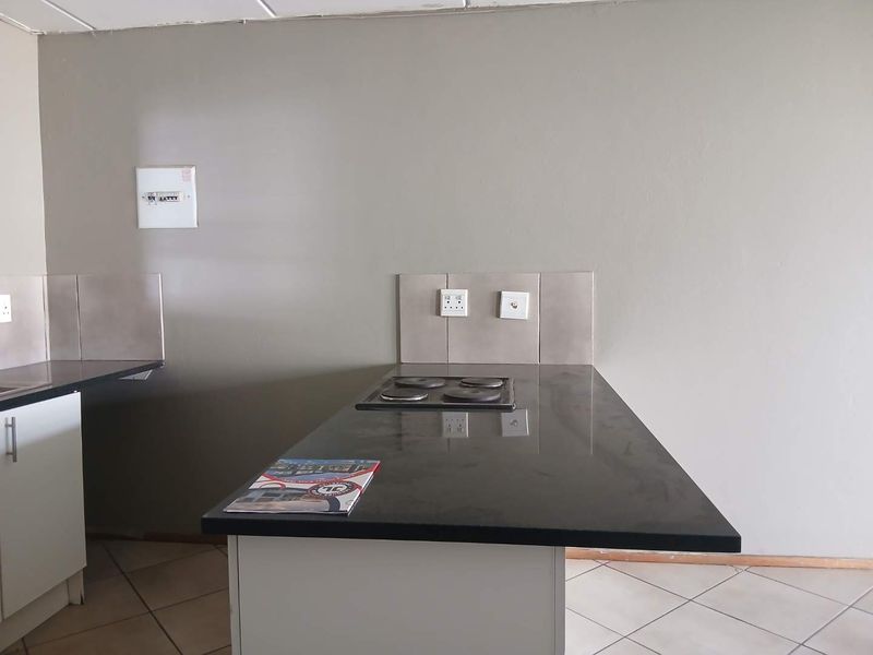 A functional kitchen area featuring a granite countertop, built-in electric hob, and tiled splashback, offering a clean and practical workspace.