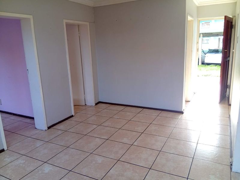 An empty living area featuring neutral ceramic floor tiles, coved ceiling cornices, and multiple doorways leading to adjacent rooms.