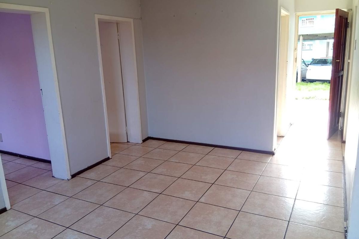 An empty living area featuring neutral ceramic floor tiles, coved ceiling cornices, and multiple doorways leading to adjacent rooms.
