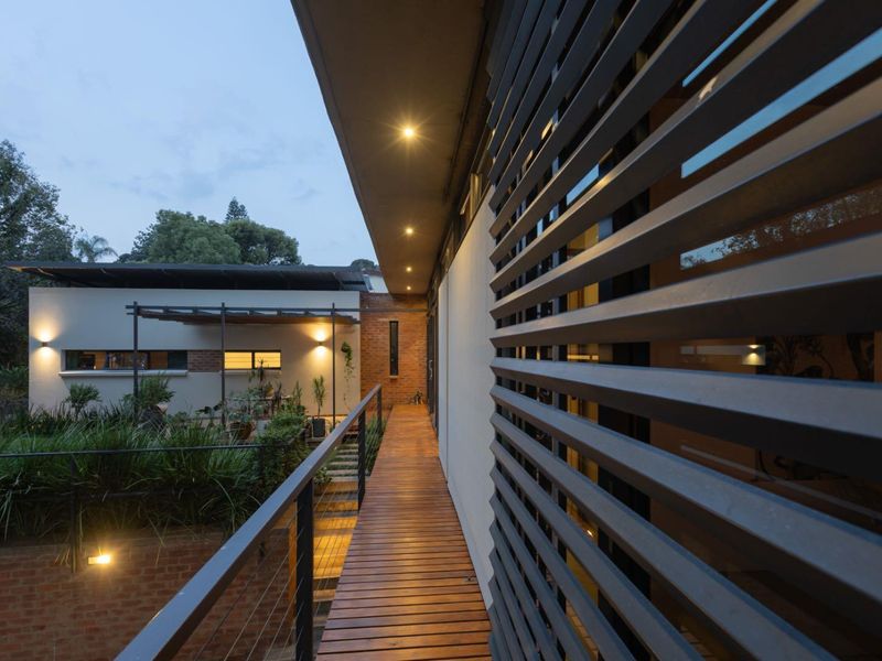 A modern elevated timber balcony featuring sleek metal balustrades, fixed exterior louvres, and recessed lighting, overlooking a landscaped garden area.