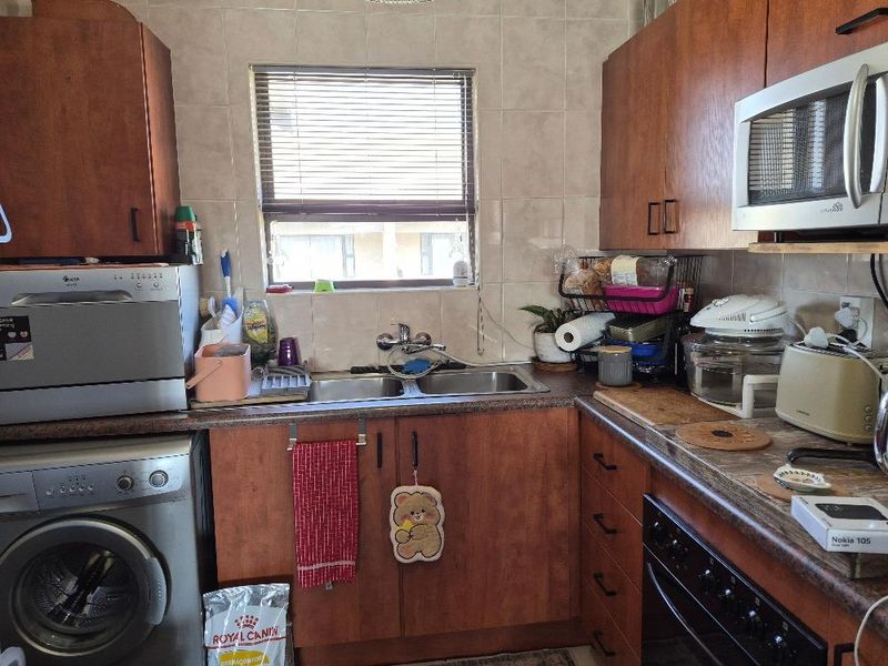 A functional kitchen featuring wooden cabinetry, laminate countertops, a double basin sink, and built-in appliances including an oven and microwave.
