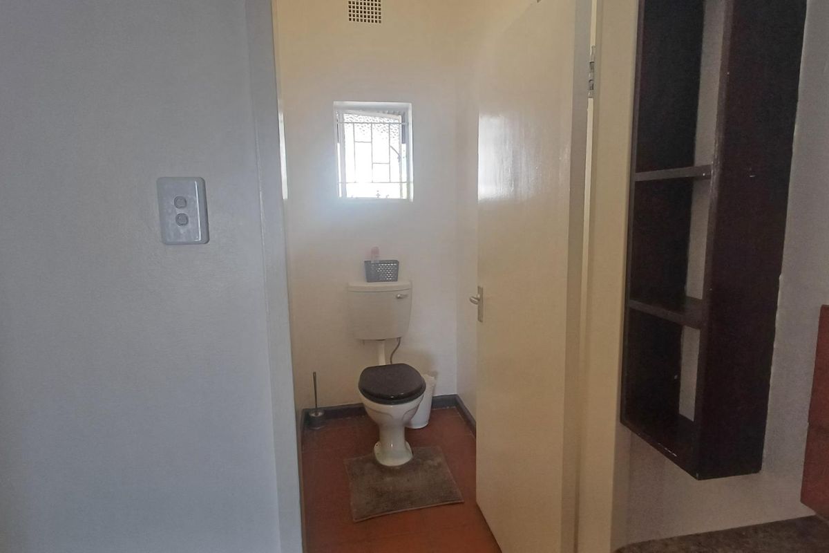A compact bathroom featuring a standard toilet, built-in shelving, and tiled flooring, requiring cosmetic updates to modernize the space.