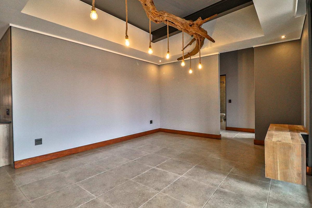 A spacious, modern living area featuring large format floor tiles, a unique driftwood pendant light fixture, and a neutral color palette.