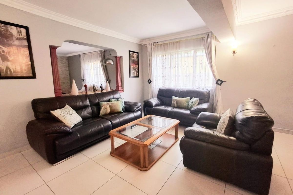 A spacious living room featuring tiled flooring, decorative ceiling cornices, and a distinctive architectural archway connecting to an adjacent space.