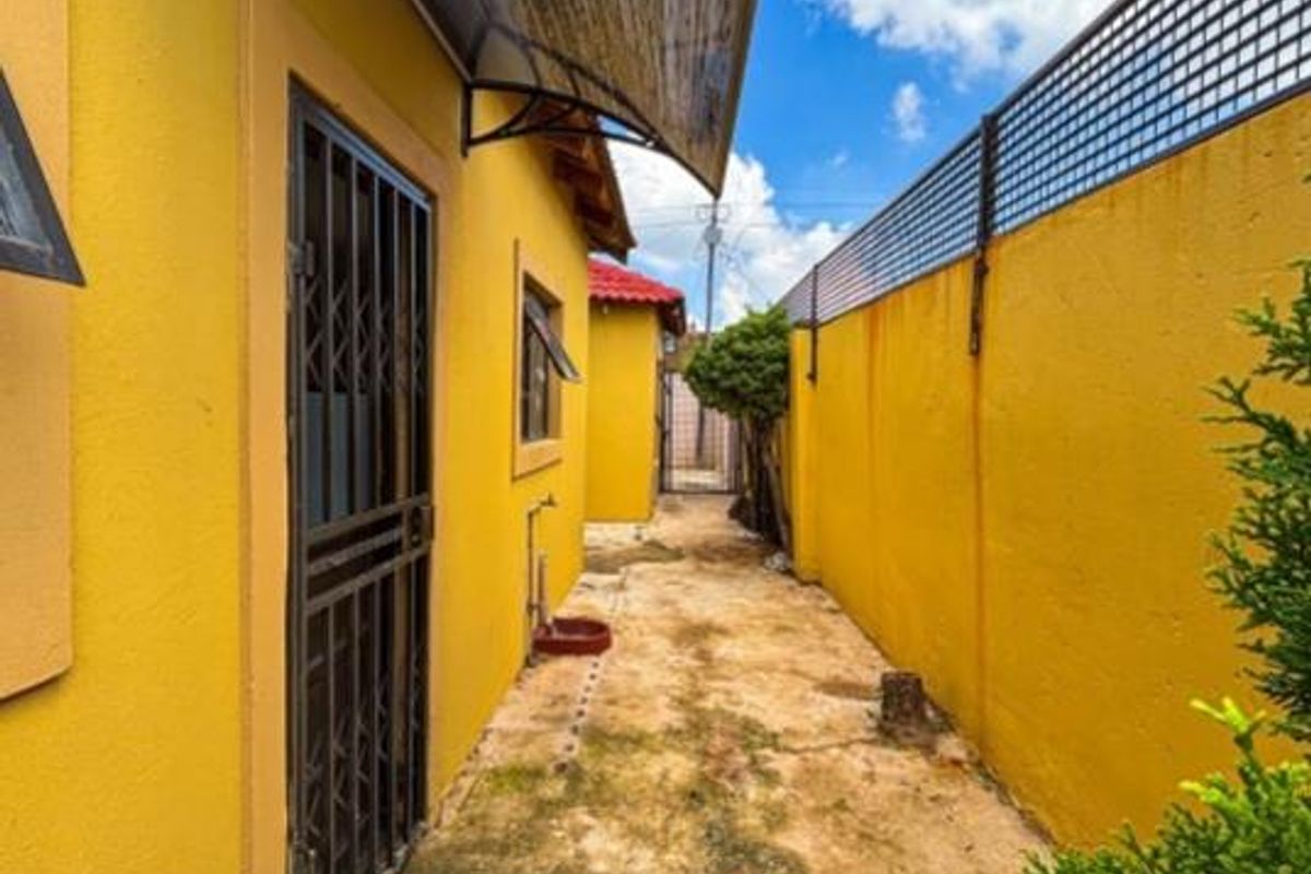 A narrow side exterior passage featuring yellow painted walls, a metal security gate, and a protective awning over the entrance.