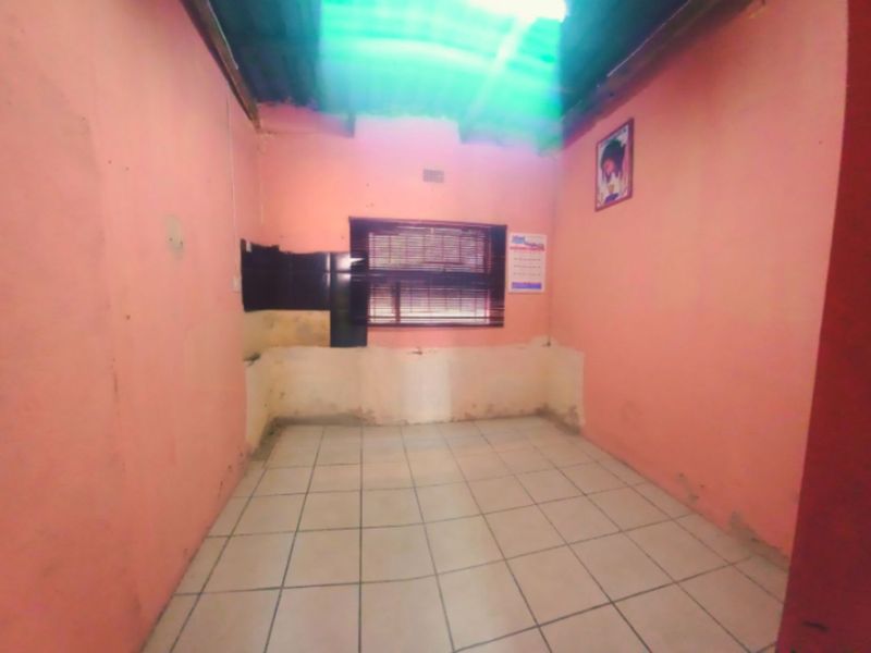 An empty, unfinished kitchen space featuring tiled flooring, a window with blinds, and exposed roof structure, requiring significant renovation and finishing.