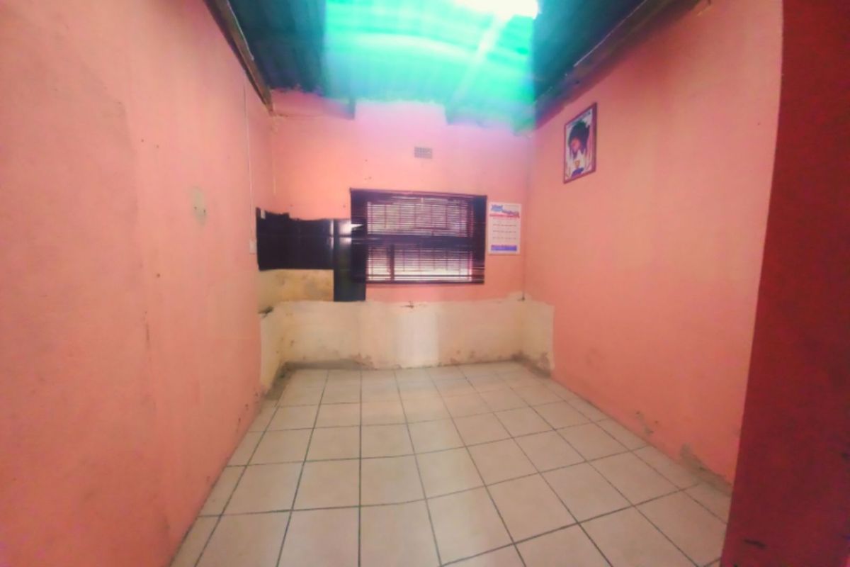 An empty, unfinished kitchen space featuring tiled flooring, a window with blinds, and exposed roof structure, requiring significant renovation and finishing.