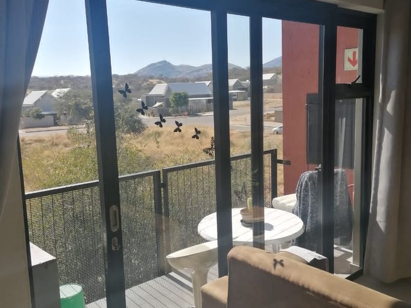 A balcony featuring a metal mesh balustrade and sliding glass door access, offering views of the surrounding neighbourhood and distant hills.