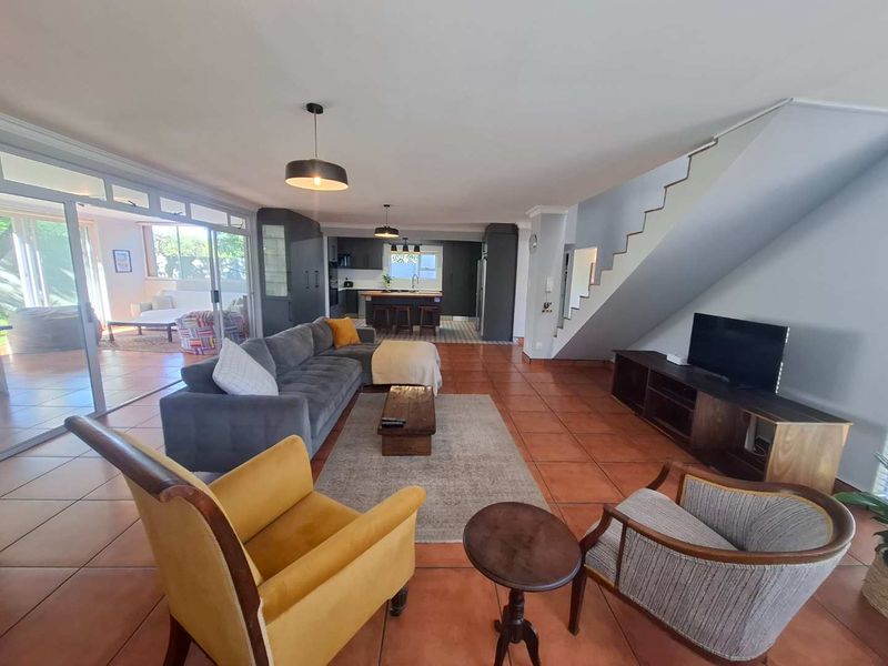 Spacious open-plan living area featuring terracotta floor tiles, a staircase, and a modern kitchen with a central island and sliding doors to the patio.