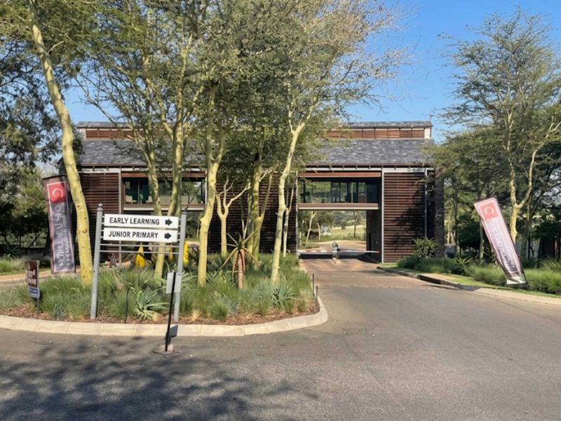 The entrance to the residential estate features a modern security gatehouse, paved driveway, and well-maintained landscaped surroundings.