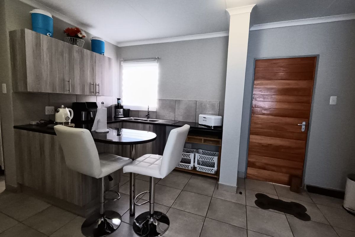 A functional kitchen featuring wood-look cabinetry, dark countertops, tiled backsplash, and a breakfast bar area with tiled flooring.