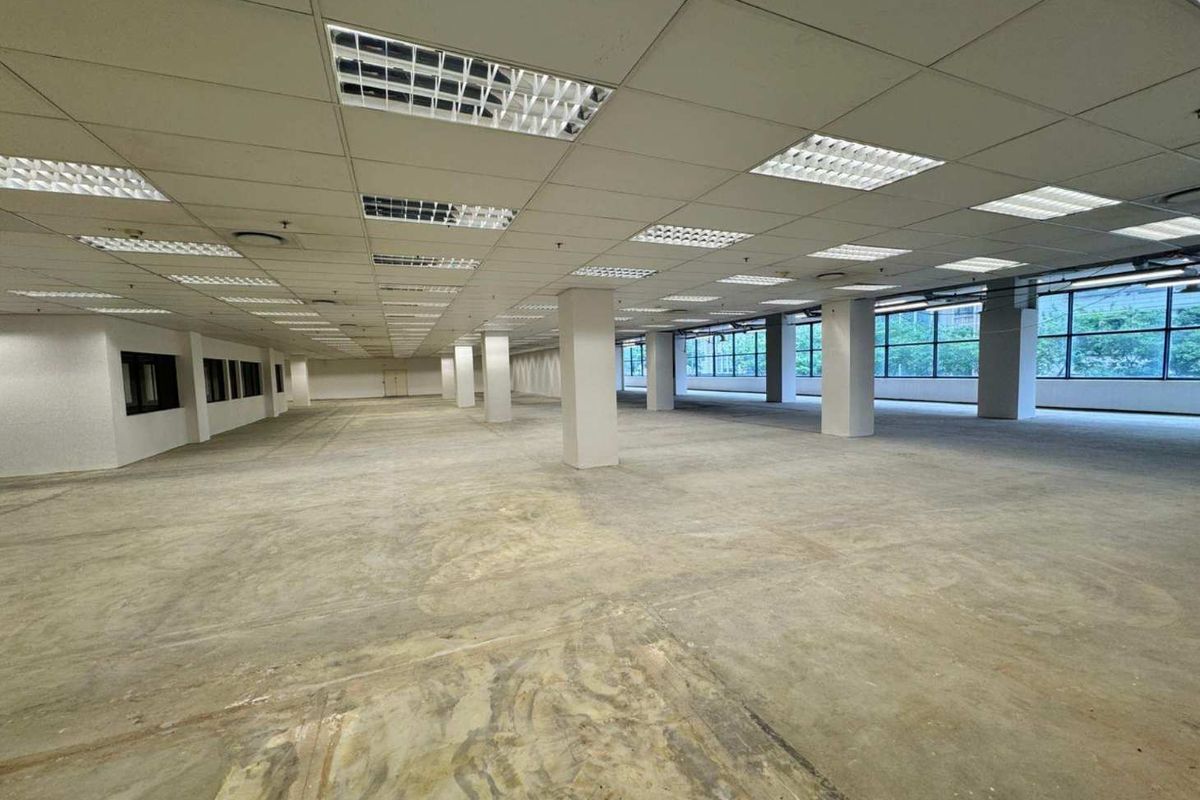Expansive open-plan retail or office space featuring a suspended ceiling, recessed lighting, concrete flooring, and large windows providing ample natural light.