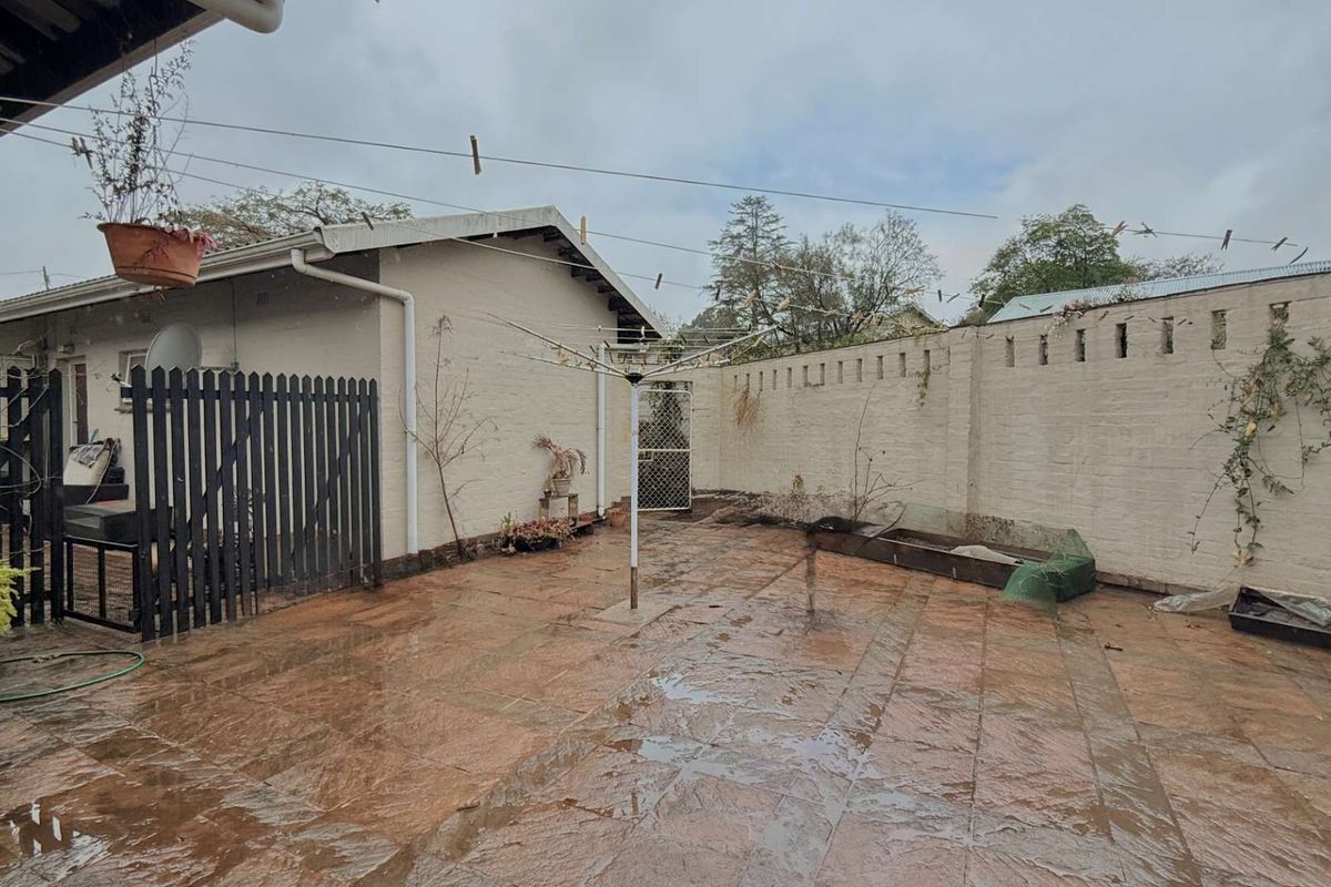 A paved rear courtyard area featuring perimeter brick walls and a metal security gate, offering a functional outdoor space with potential for landscaping.