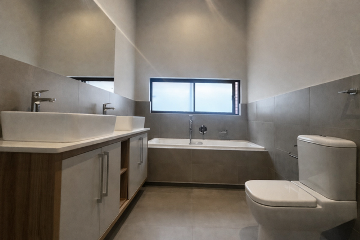 Modern bathroom featuring a double vanity with vessel sinks, a built-in bathtub, and a contemporary toilet, finished with neutral wall and floor tiles.