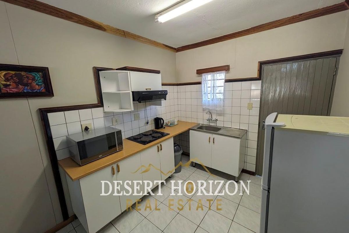 Compact kitchen featuring white cabinetry, tiled splashbacks, a built-in hob, and a stainless steel sink unit.