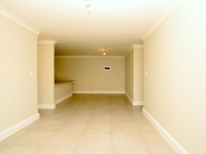 An empty open-plan living and kitchen area featuring neutral walls, tiled flooring, and a breakfast bar counter.