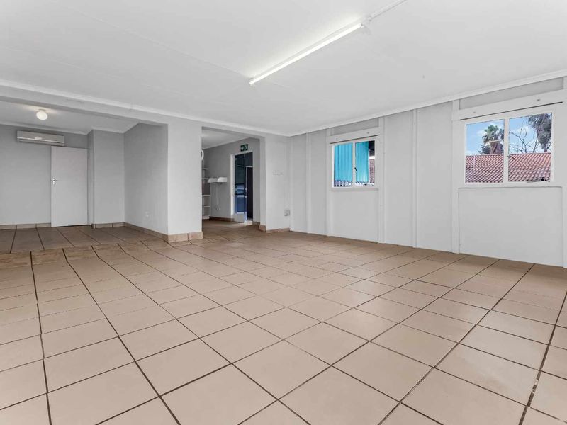 A spacious, empty living area featuring neutral tiled flooring, bright overhead lighting, and split-system air conditioning, offering a versatile blank canvas.