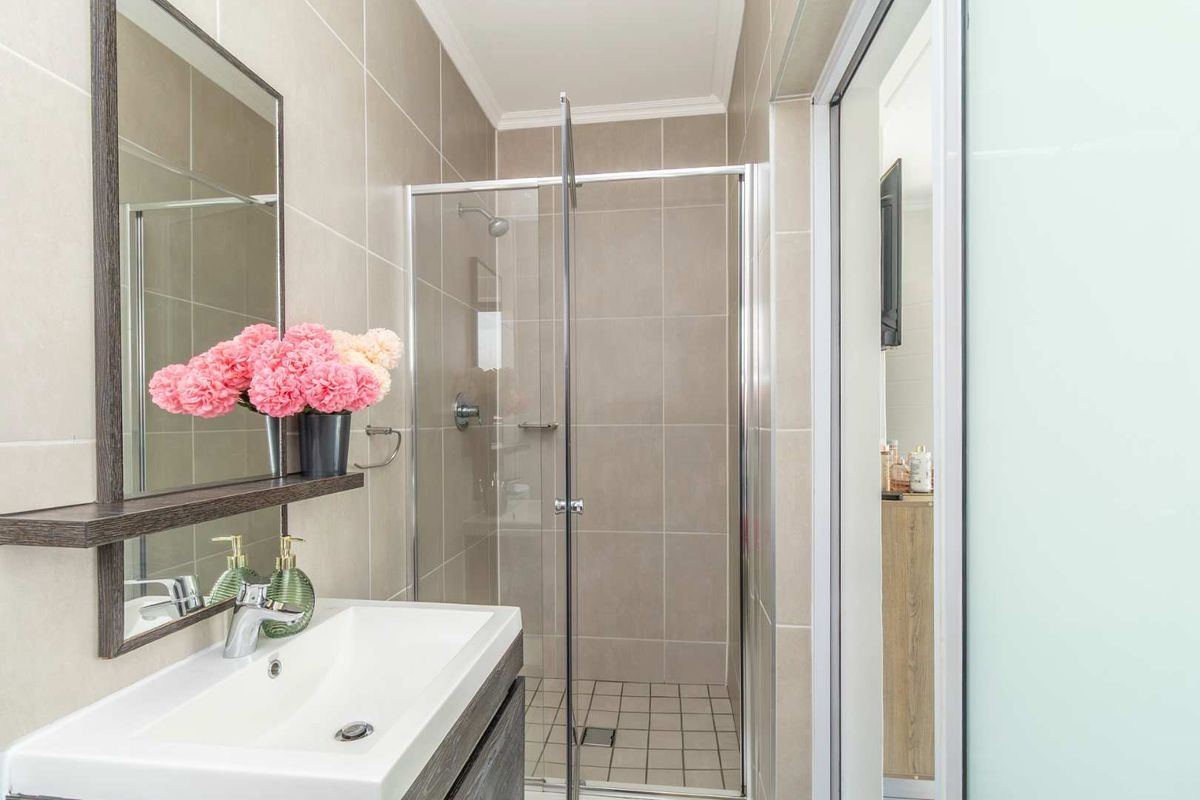 Modern bathroom featuring a vanity with basin, wall-mounted mirror, and a glass-enclosed shower with neutral wall tiling.