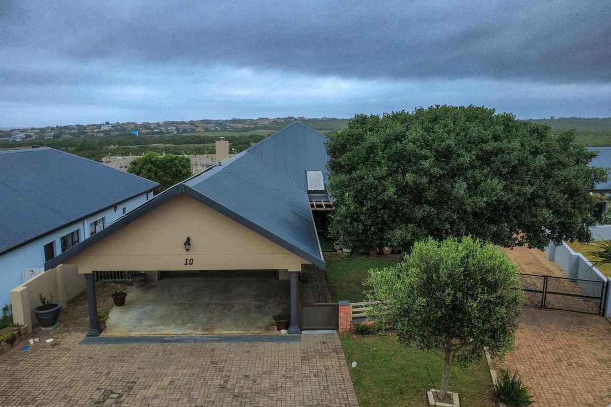 Aerial view of the property featuring a paved driveway, covered carport, and established garden area under a pitched metal roof.