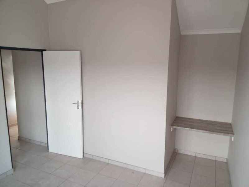 A clean, empty bedroom featuring neutral wall tones, tiled flooring, and a convenient built-in desk area.