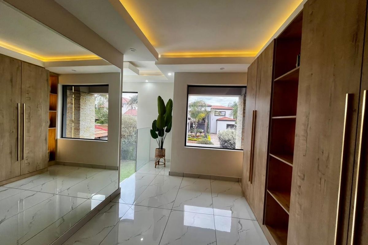 Modern bedroom featuring floor-to-ceiling built-in wooden cabinetry, large mirrored wardrobe doors, polished marble-look floor tiles, and recessed cove lighting.