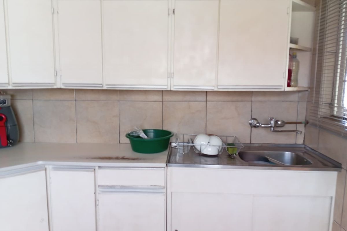 A functional kitchen area featuring white cabinetry, a stainless steel sink with wall-mounted faucet, and tiled splashback.