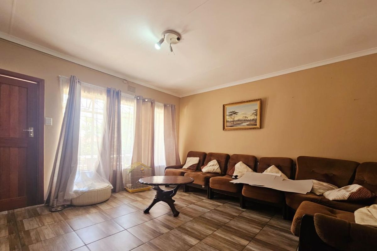 A living room featuring tiled flooring, large windows with curtains, and a central ceiling light fixture.