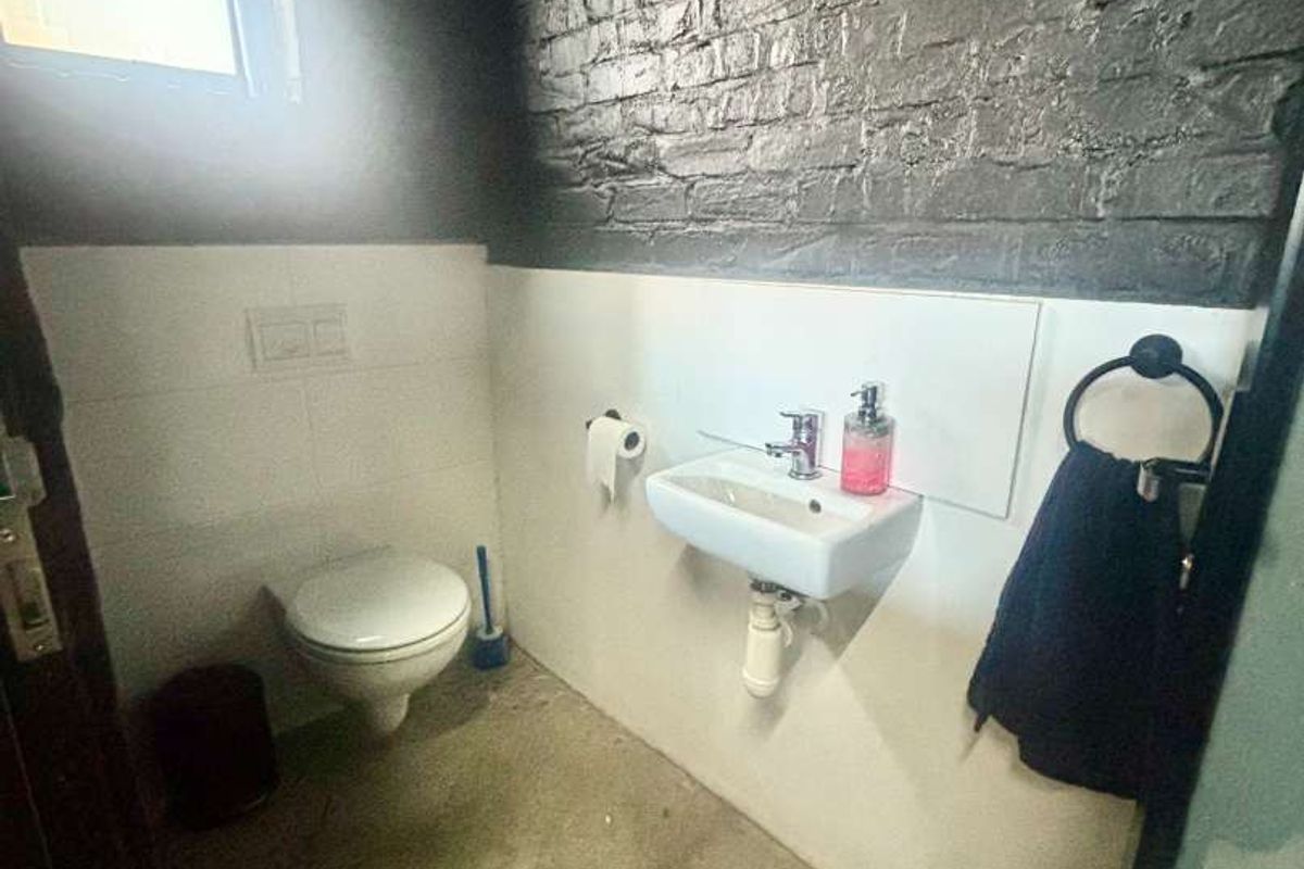 A compact bathroom featuring a wall-mounted toilet, basin, and exposed brick wall with concrete flooring, offering potential for modern renovation.