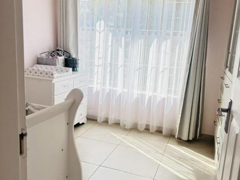 A bedroom featuring tiled flooring, a ceiling fan, and built-in cupboards, with large windows fitted with security bars for added safety.