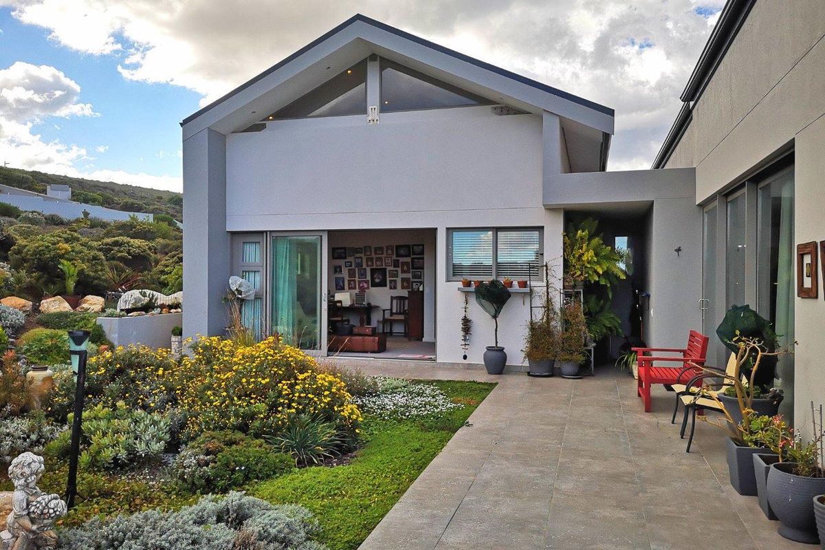 Rear view of the property featuring a paved patio area, landscaped garden, and modern architectural design with large sliding doors and gable roof.