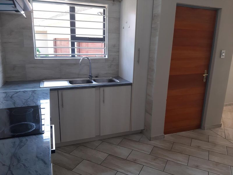 A clean, modern kitchen featuring stone-look countertops, a double sink, electric hob, extractor fan, and tiled flooring with a timber door.