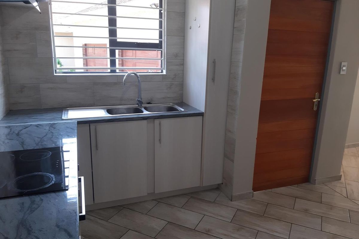 A clean, modern kitchen featuring stone-look countertops, a double sink, electric hob, extractor fan, and tiled flooring with a timber door.