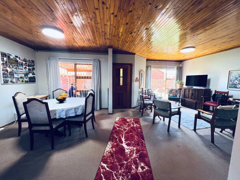 Spacious open-plan living and dining area featuring a distinctive timber-paneled ceiling, neutral walls, and sliding glass doors providing access to the outdoor space.